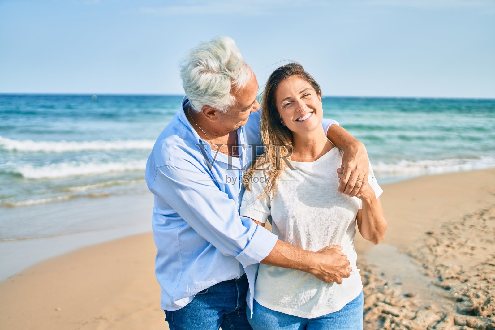 一对中年西班牙夫妇微笑着拥抱在海滩上散步照片摄影图片