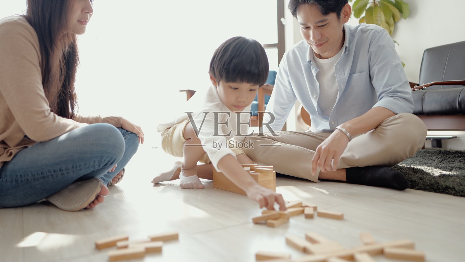 快乐的亚洲年轻父母,爸爸妈妈看着儿子玩玩具坐在家里的地板上。有爱心的父亲和母亲,有乐趣帮助可爱的小男孩建造木塔。给客厅享受游戏活动。照片摄影图片