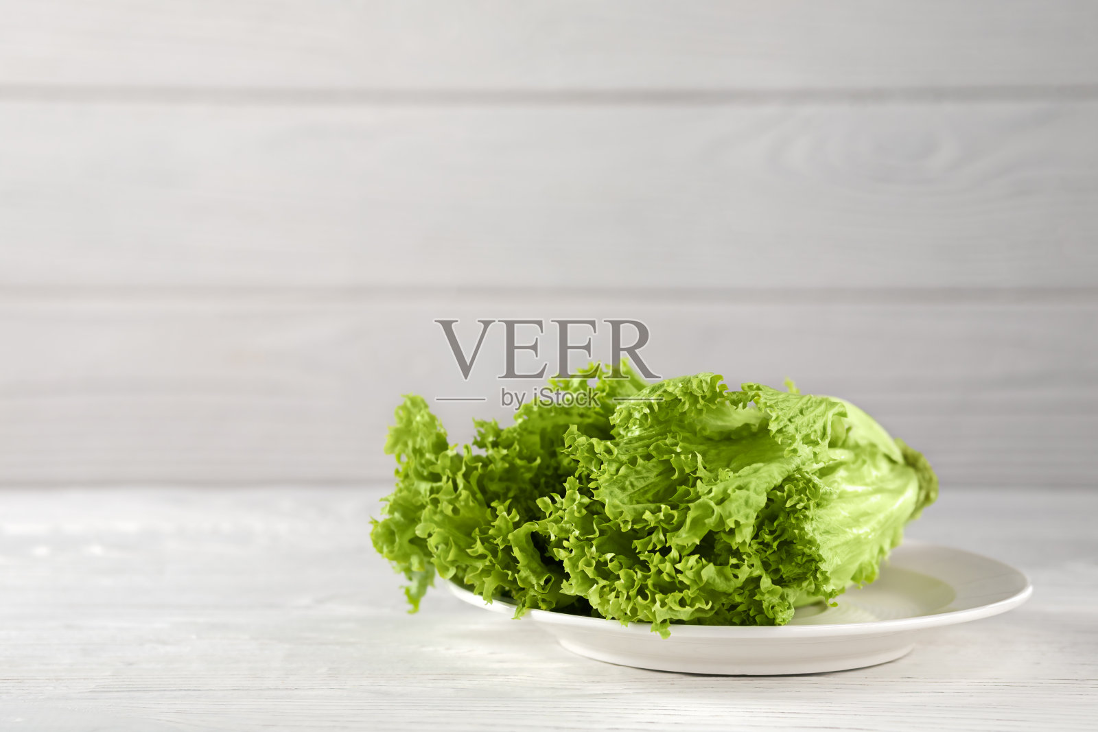 新鲜的生菜叶放在一个木制背景的浅盘上。膳食营养照片摄影图片