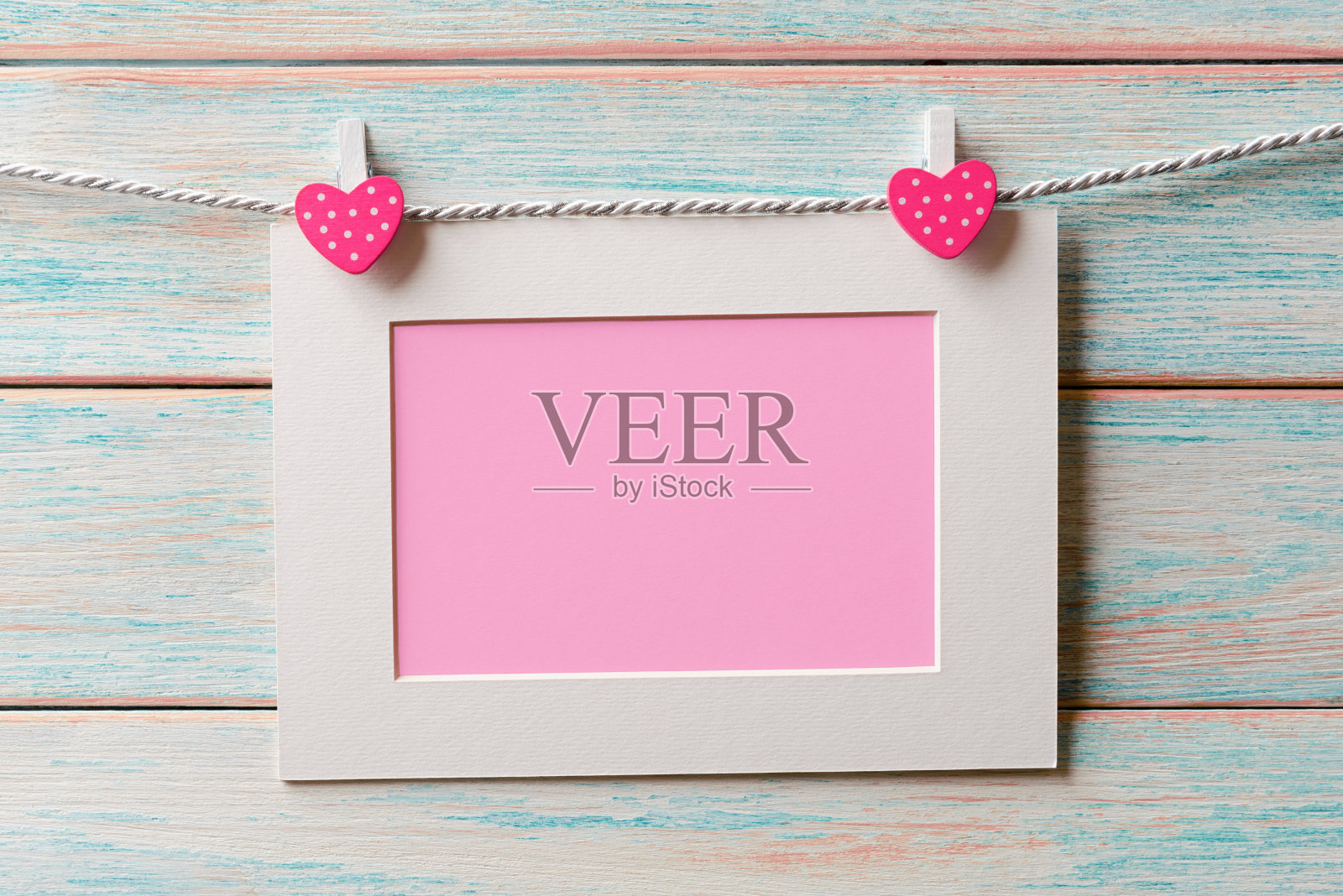粉红色的空白卡片在白色的框架上挂在一根绳子在木制的背景上。有拷贝空间的情人节卡片照片摄影图片