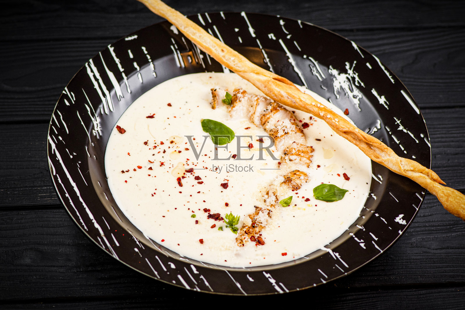 芝士鸡汤配格里西尼面包条,装在木制背景的黑色碗里。照片摄影图片