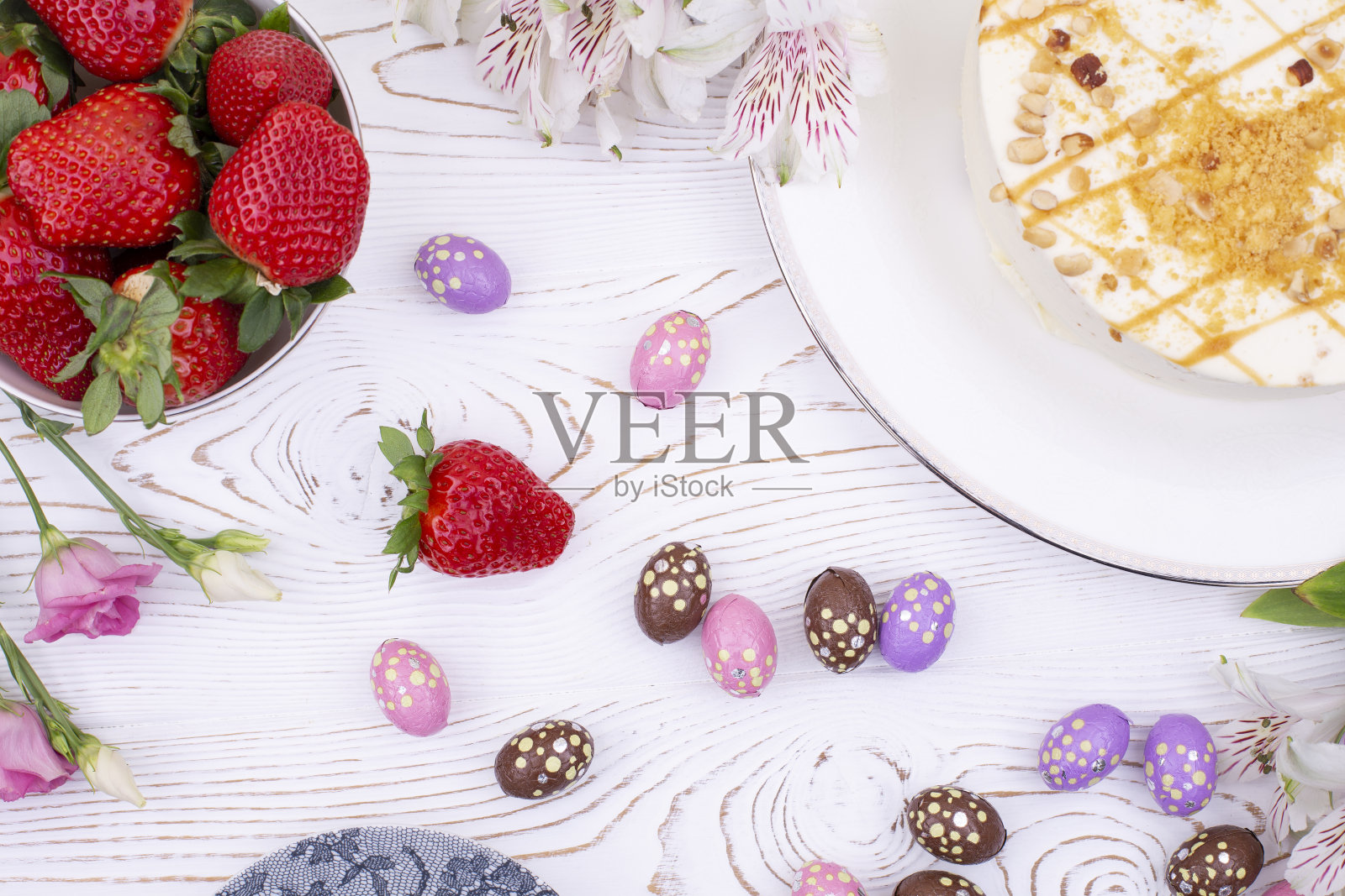复活节蛋糕上面点缀着白色奶油、坚果、草莓和巧克力蛋,还有五颜六色的包装纸和春天的花朵照片摄影图片