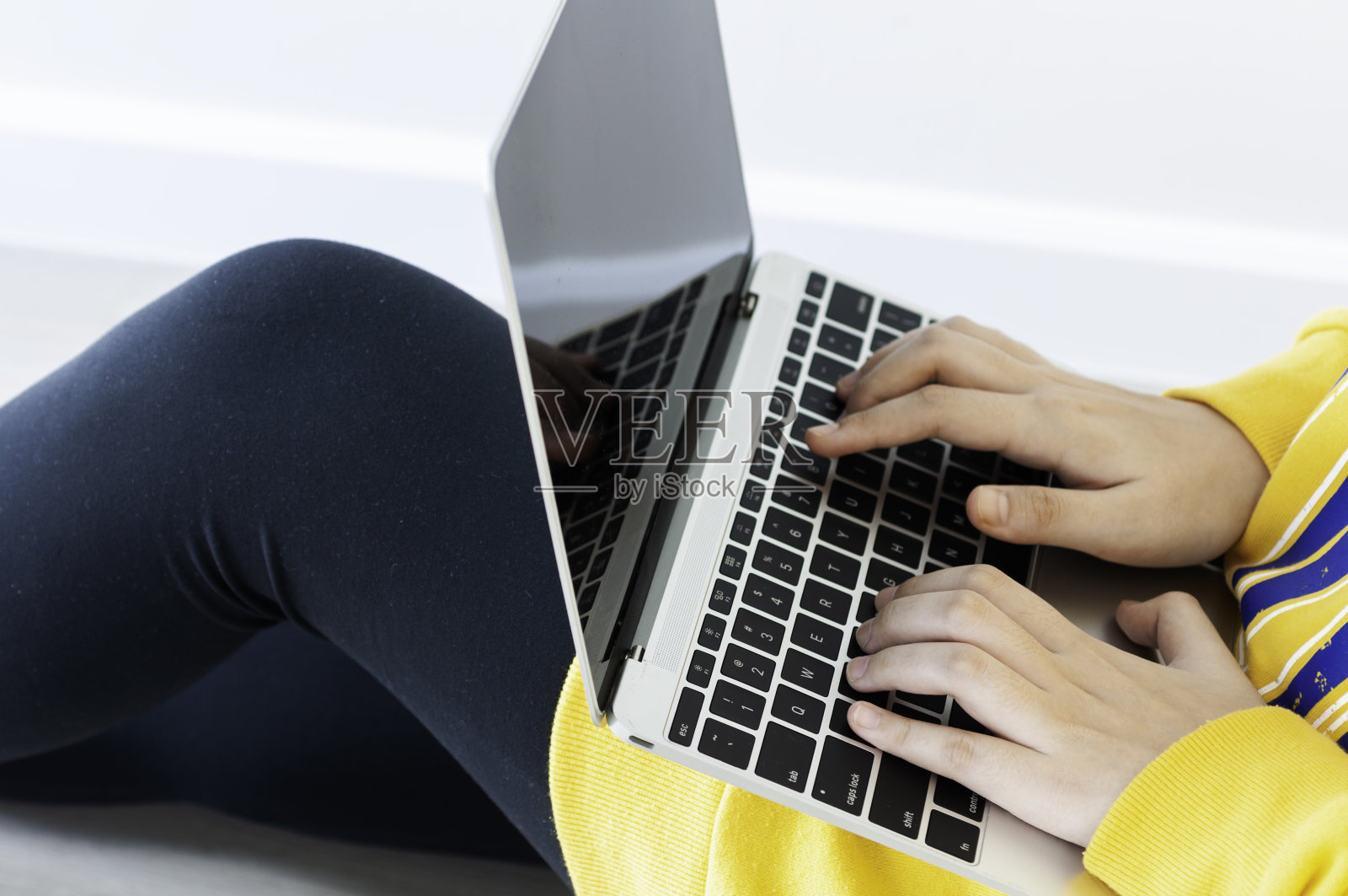 冠状病毒危机期间,亚洲女青少年用18岁的笔记本电脑在家做在线学习,在冠状病毒危机期间,穿着休闲黄色布的女性在家里使用笔记本电脑工作。泰国。照片摄影图片