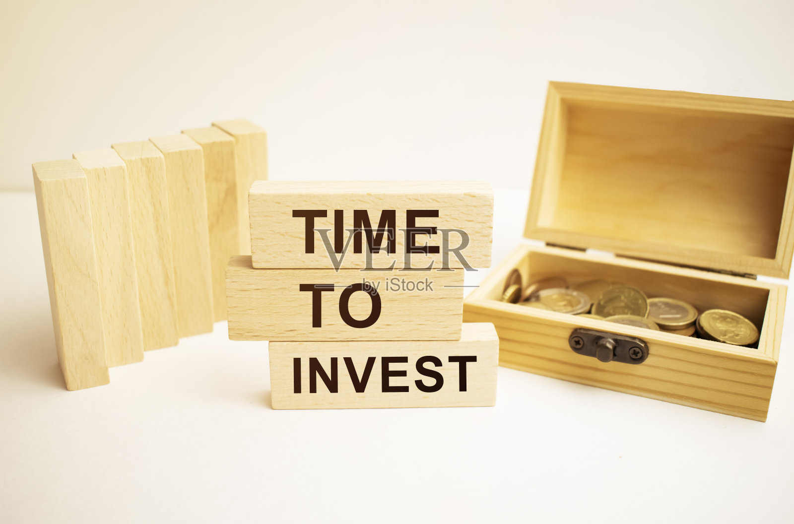 invest这个词用英语写在木块上。一个储蓄罐,一个红色的钟和硬币组成的图像。照片摄影图片