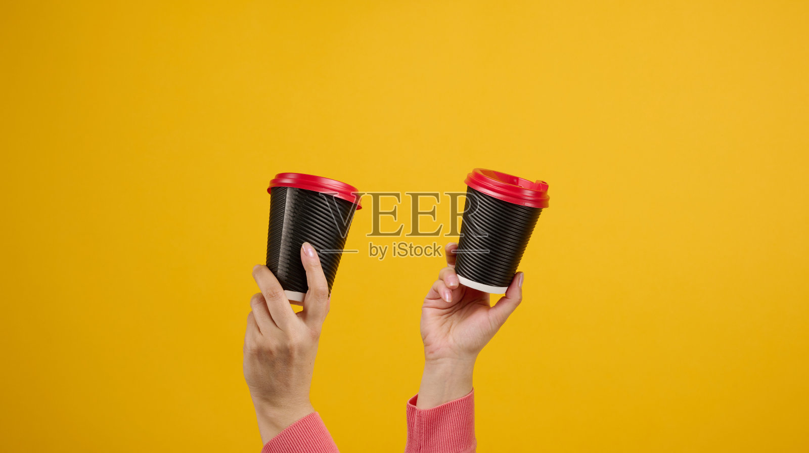 手里拿着棕色的硬纸板咖啡杯,黄色的背景。环保餐具照片摄影图片