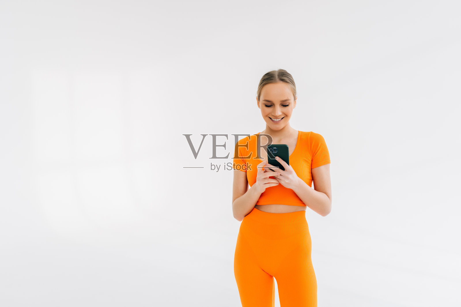 年轻的运动女性的肖像运动胸罩和打底裤使用智能手机孤立在白色背景。照片摄影图片