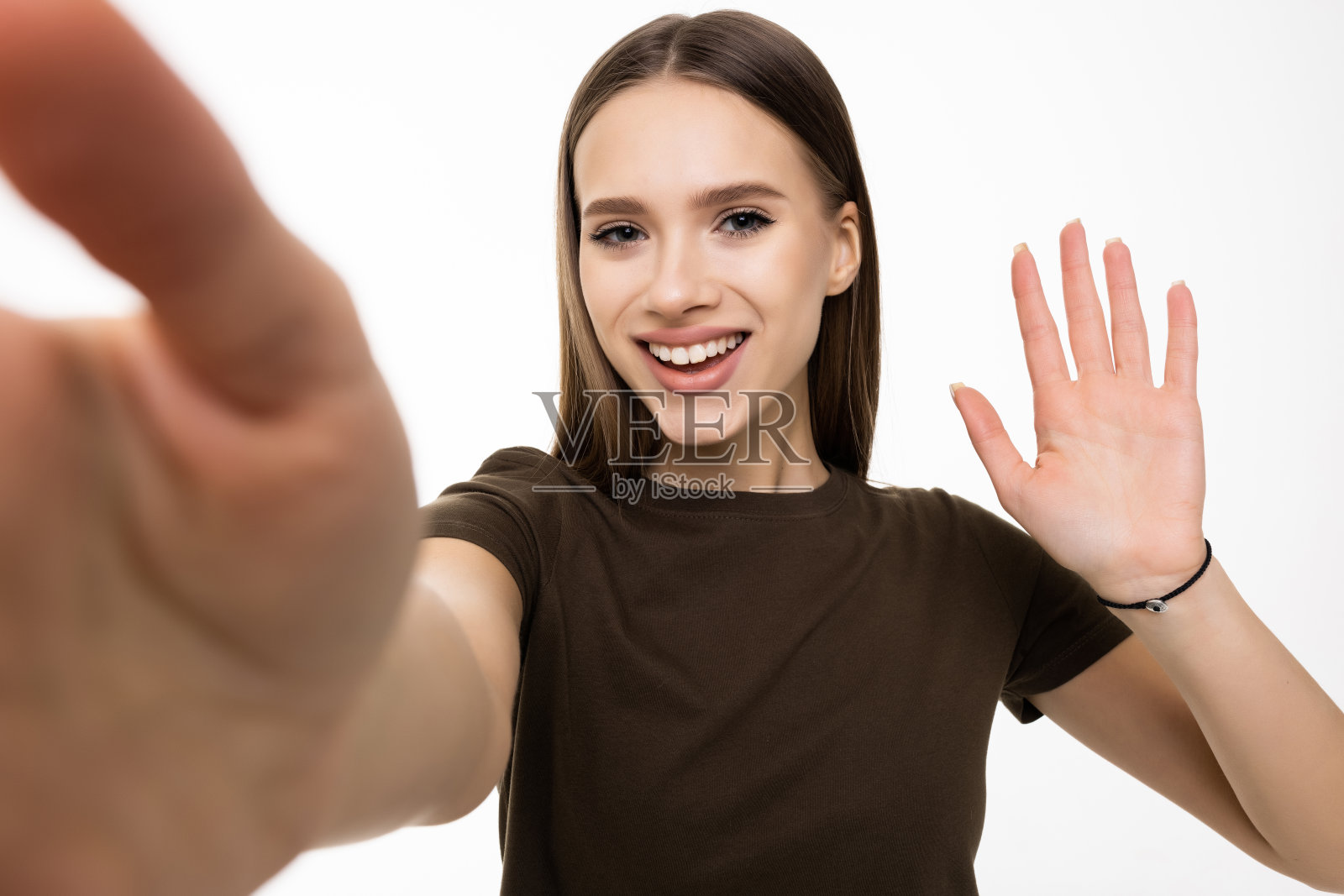 快乐的年轻女性博主网红拿着现代智能手机挥手问好。微笑的视频博主看着手机打电话,在灰色的背景上拍摄视频博主自拍照片摄影图片