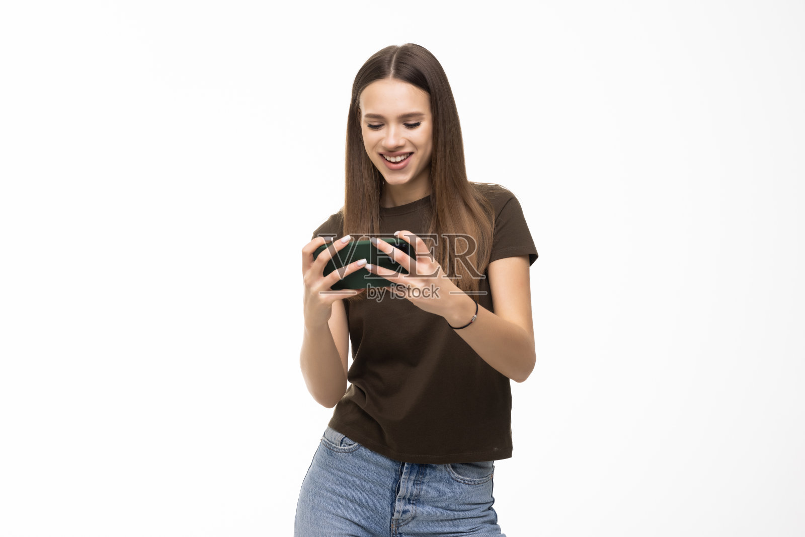 一名年轻女子在白墙背景下独自摆姿势,用手机玩游戏。照片摄影图片