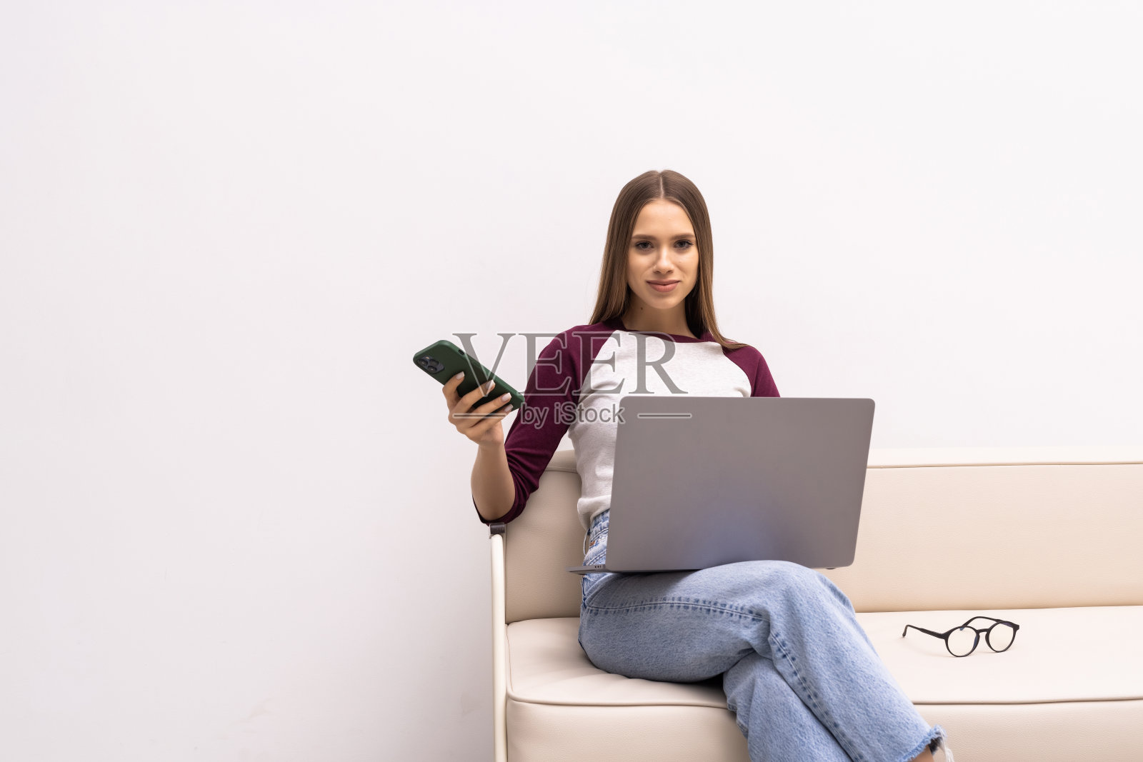 女人的肖像,拿着她的手机,在家里的沙发上微笑和愉快地交流。照片摄影图片