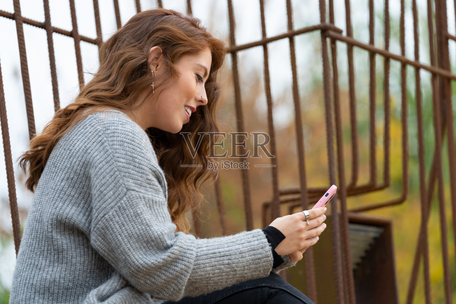 年轻的红发女人坐在公园里看着她的智能手机照片摄影图片