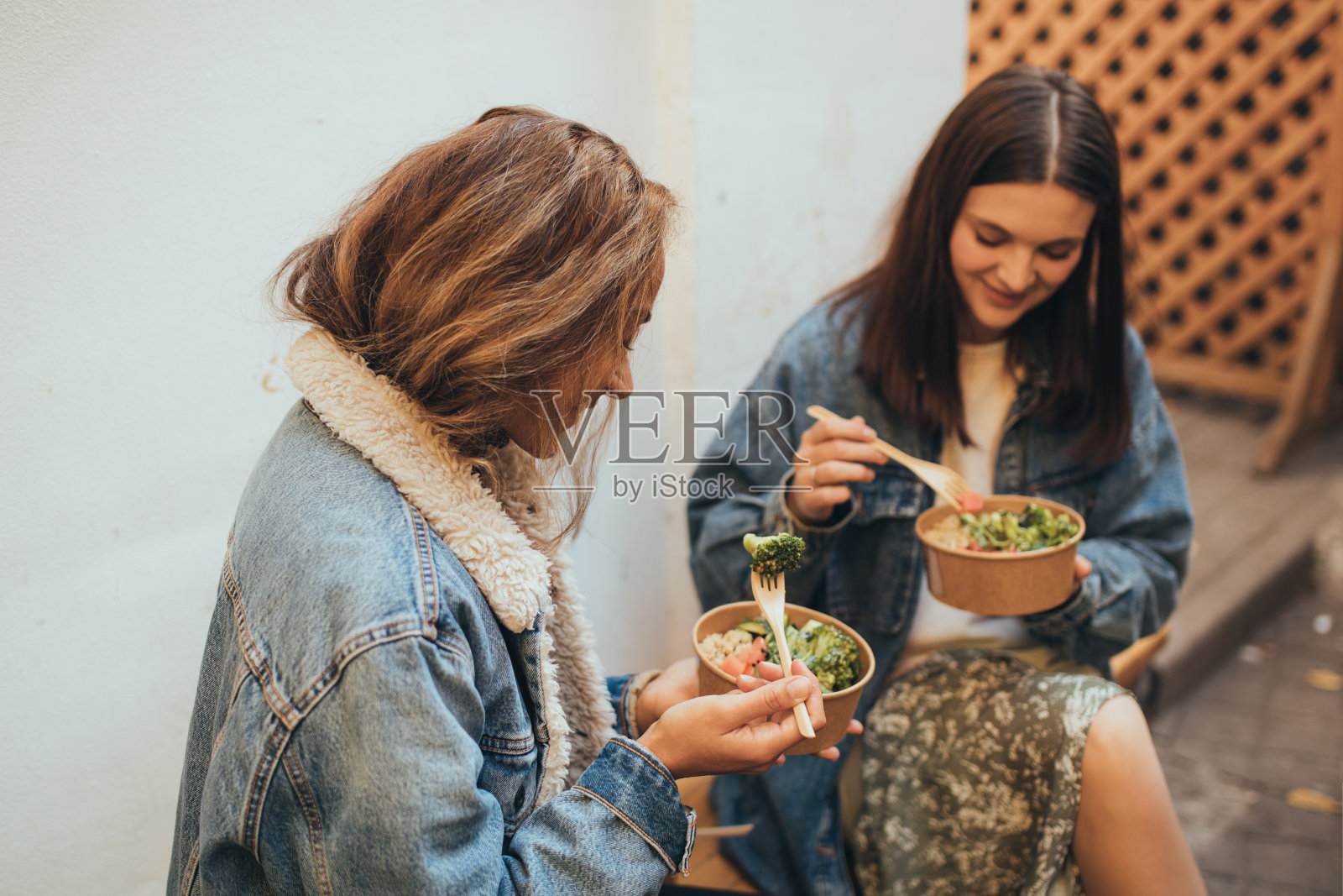 两个年轻的女性朋友坐在户外吃着外卖,笑着,玩得很开心。送餐和外卖。照片摄影图片
