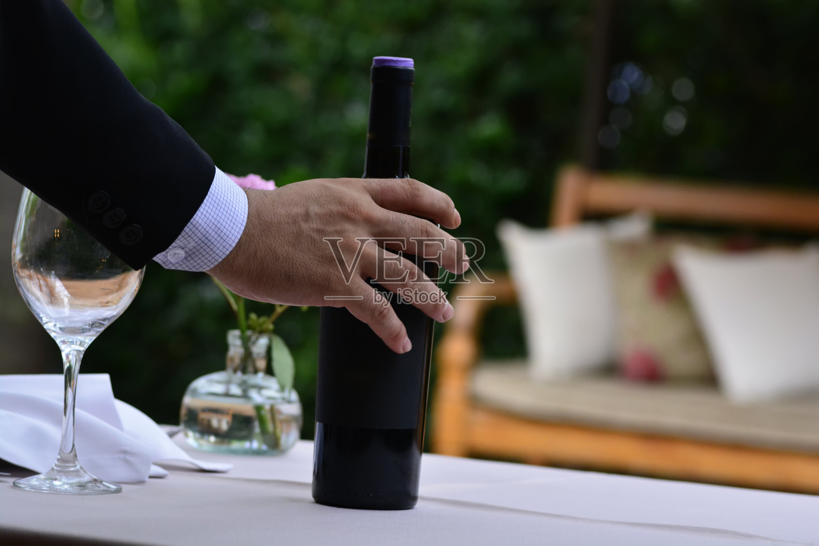 在一家以绿色花园为背景的餐厅里,侍者端上葡萄酒,侍酒师端上一瓶红酒照片摄影图片