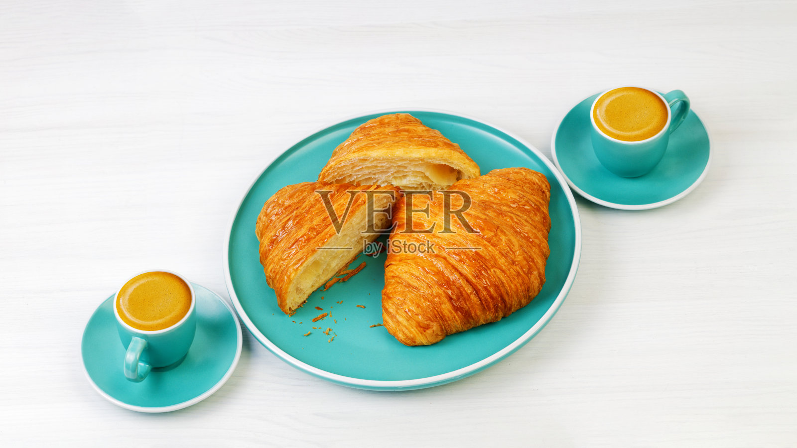 白色木桌上放着牛角面包和两杯浓缩咖啡。角度的观点。照片摄影图片