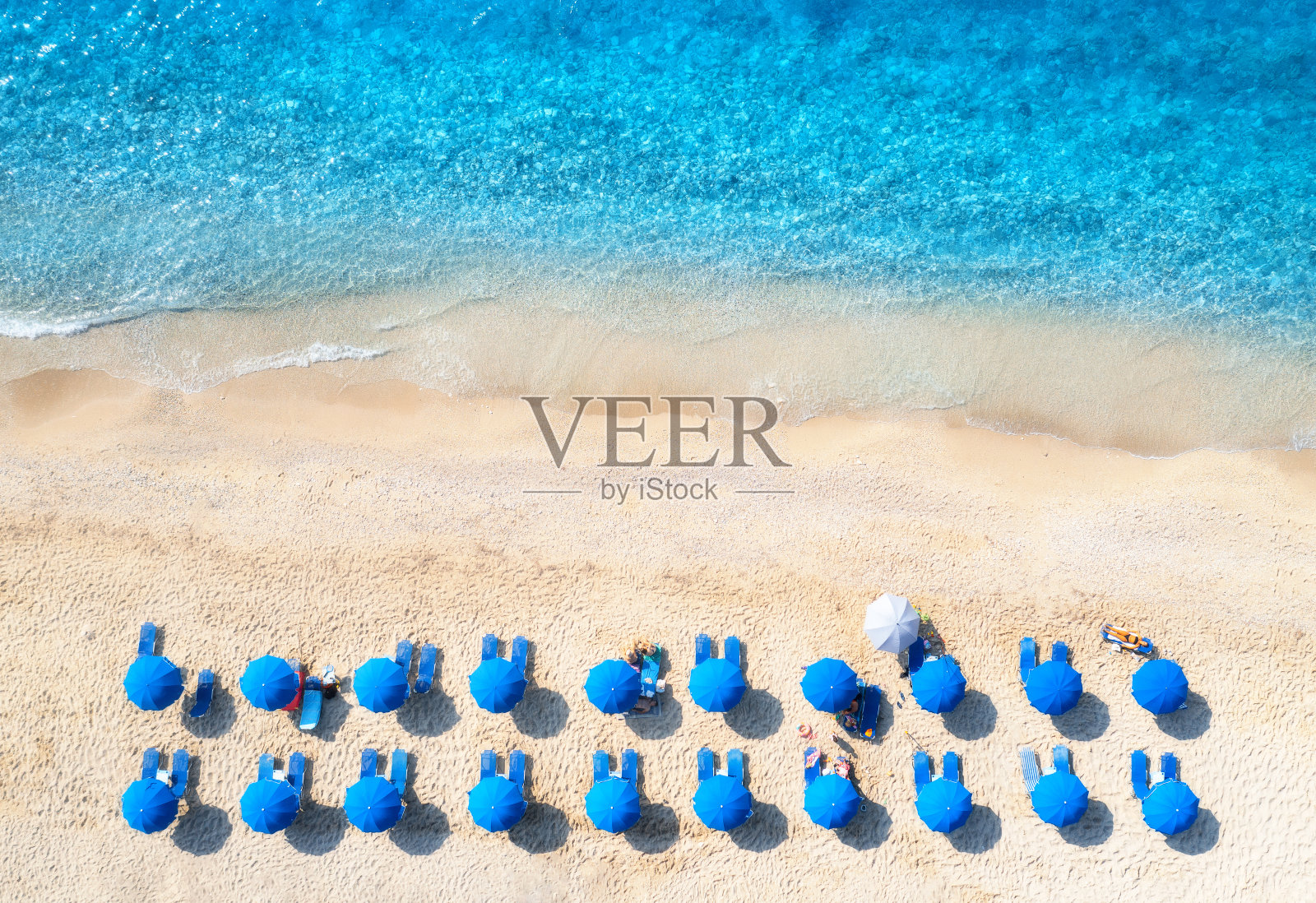 从空中俯瞰蓝色的大海,夏日日落时的沙滩和太阳床。绿松石水、人、躺椅的热带景观。旅行和度假。Lefkada岛,希腊。俯视图照片摄影图片