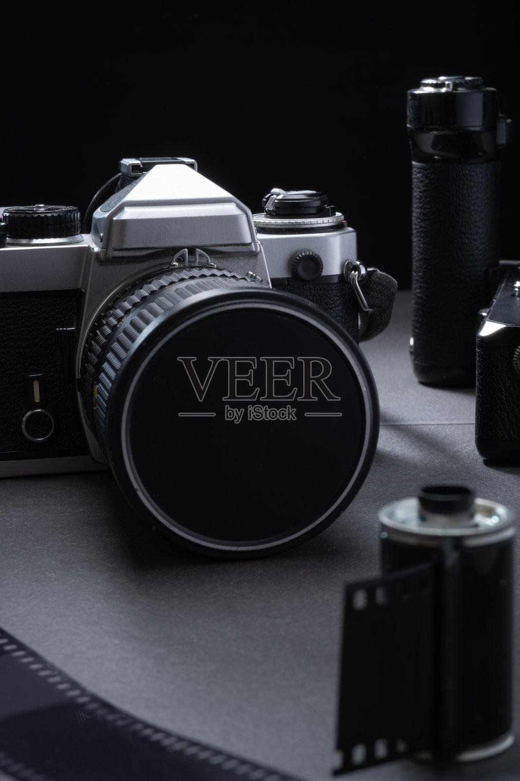 老式35mm单反相机的特写镜头,带有电池手柄。黑色背景下的旧金属膜盒。照片摄影图片