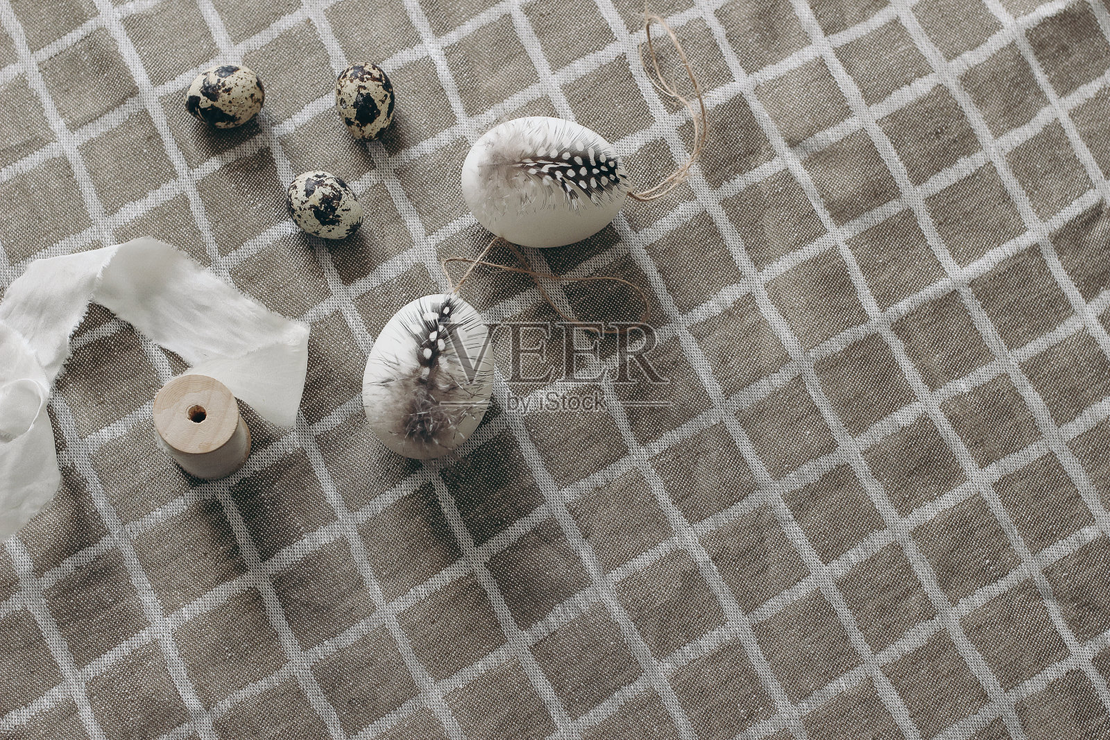 复活节装饰构图。春天的静物与天然鹌鹑和母鸡蛋装饰羽毛的珍珠鸡。格纹米色亚麻布桌布背景。丝带。中性平。照片摄影图片