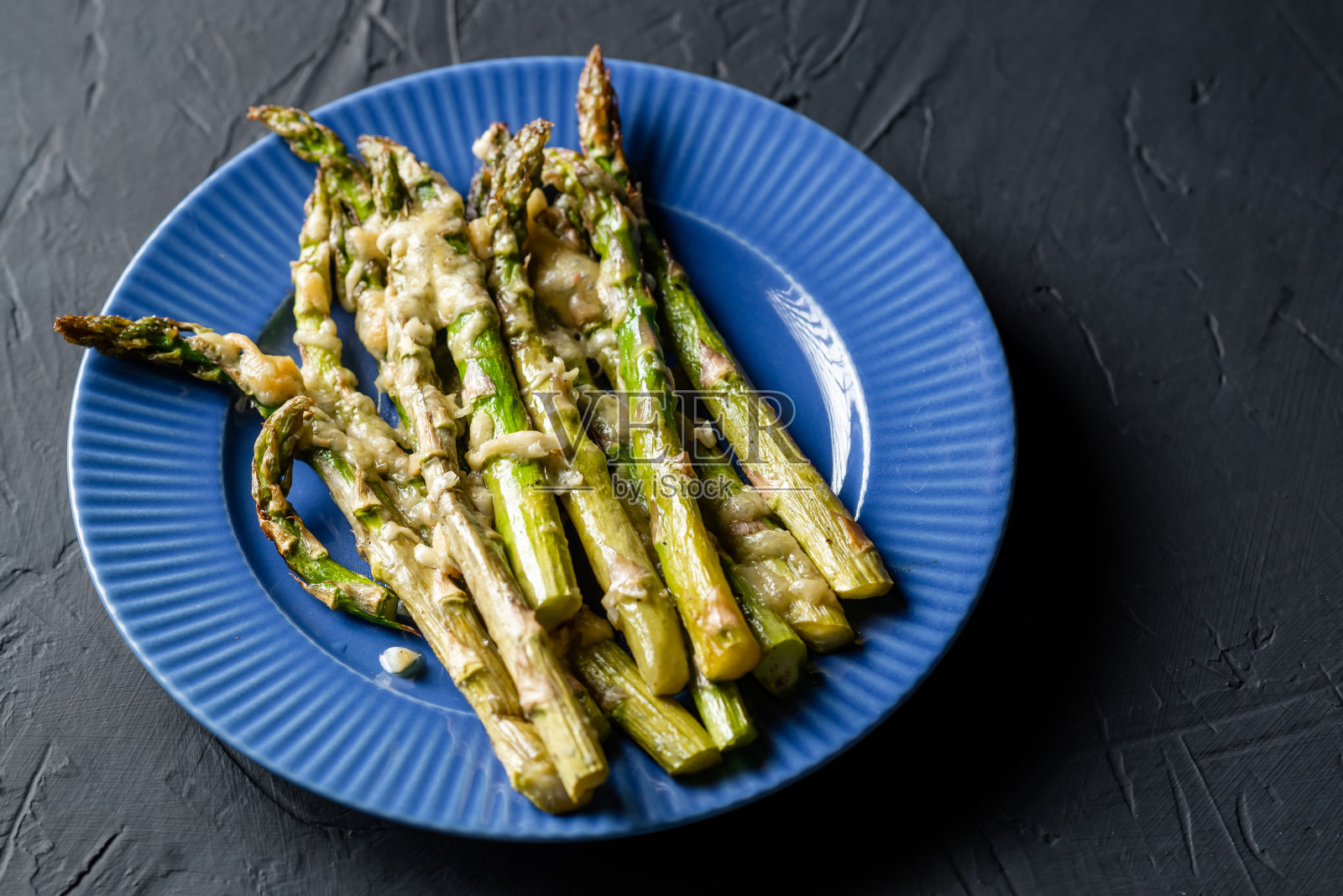用蓝色盘子烤芦笋和奶酪。黑暗的背景。素食。健康食品。照片摄影图片