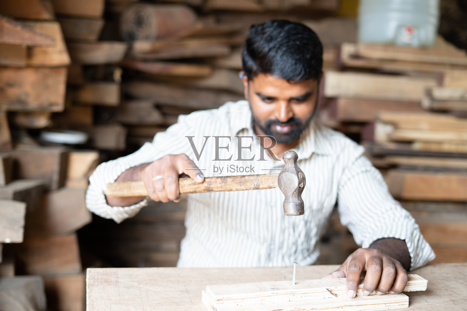 关注锤子,年轻的印度木匠在店里用锤子敲钉子,这是工匠、蓝领工作和熟练的手工劳动的概念。照片摄影图片