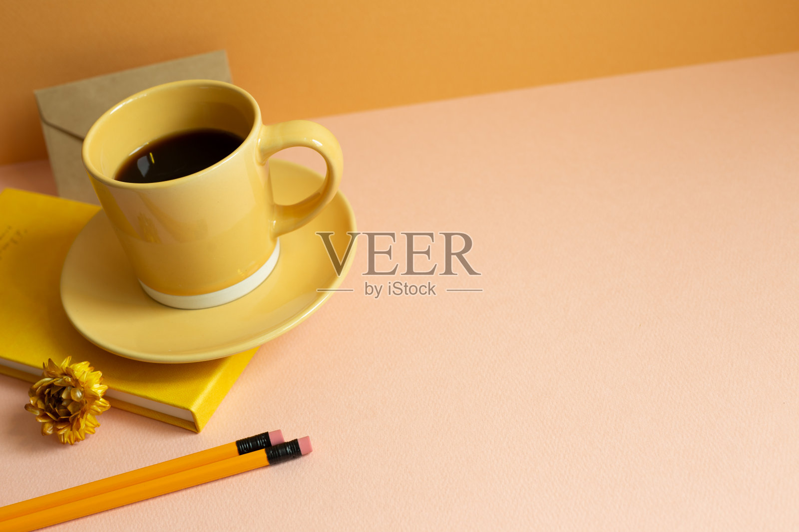 黄色的日记本,一杯咖啡,粉红色的桌子上的铅笔。橙色的背景墙。本空间照片摄影图片