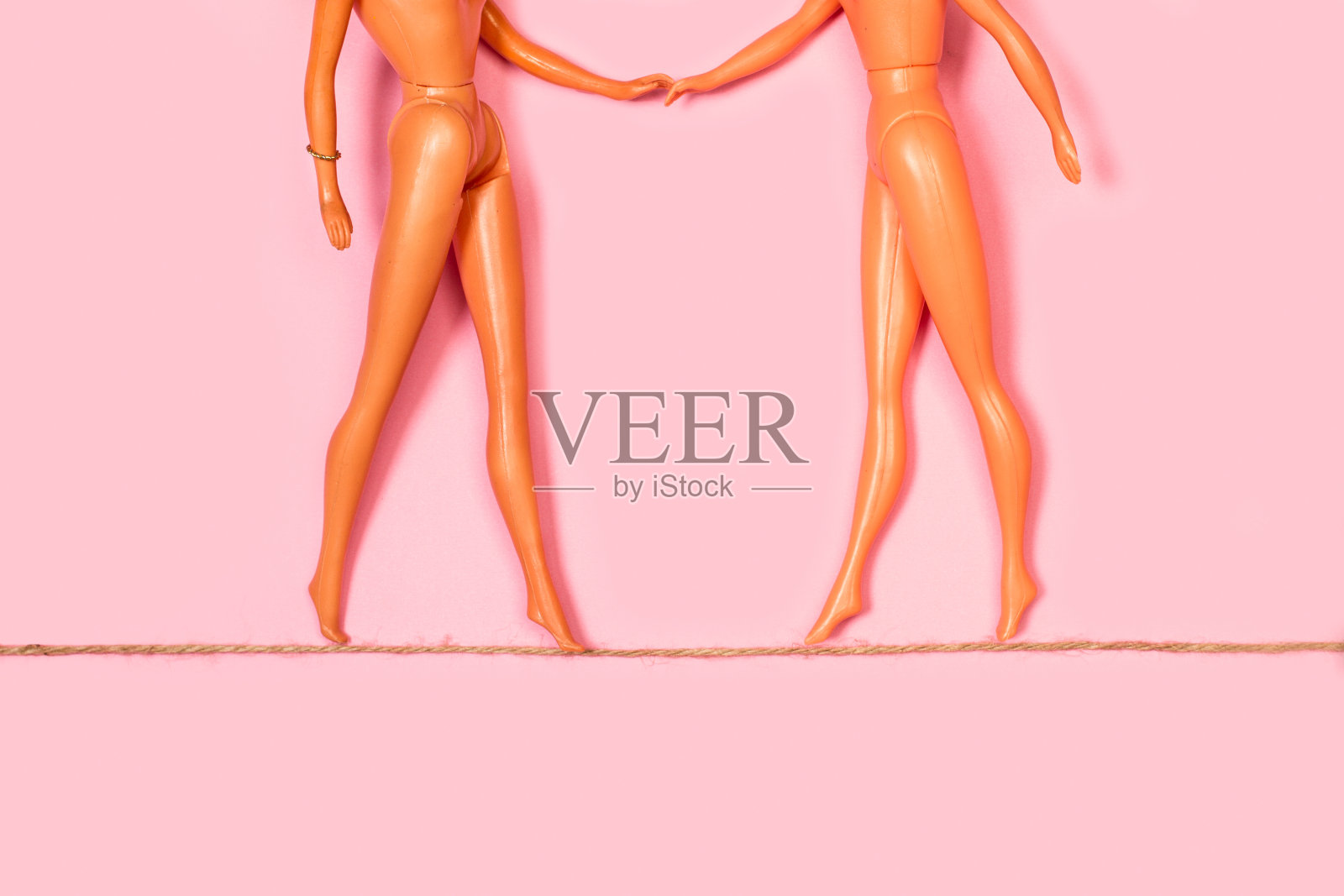 两个娃娃在粉红色的背景上牵着手走在绳子上照片摄影图片