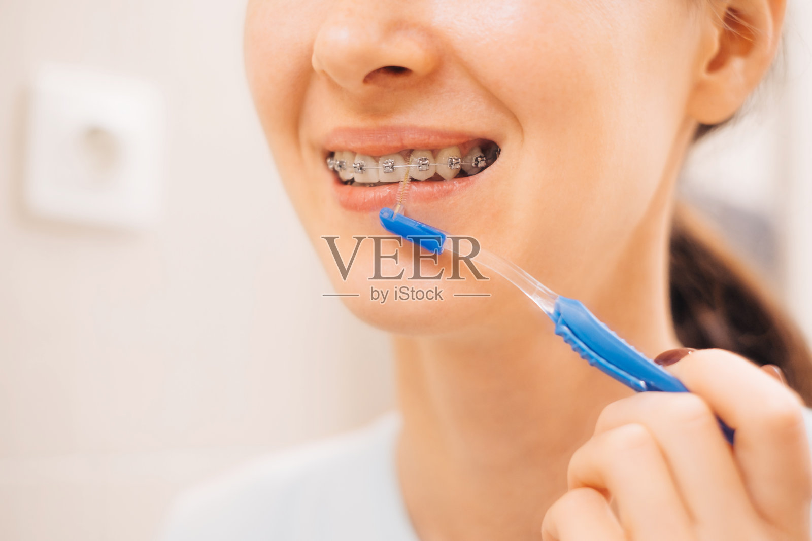 年轻女子戴着牙套刷牙。照片摄影图片