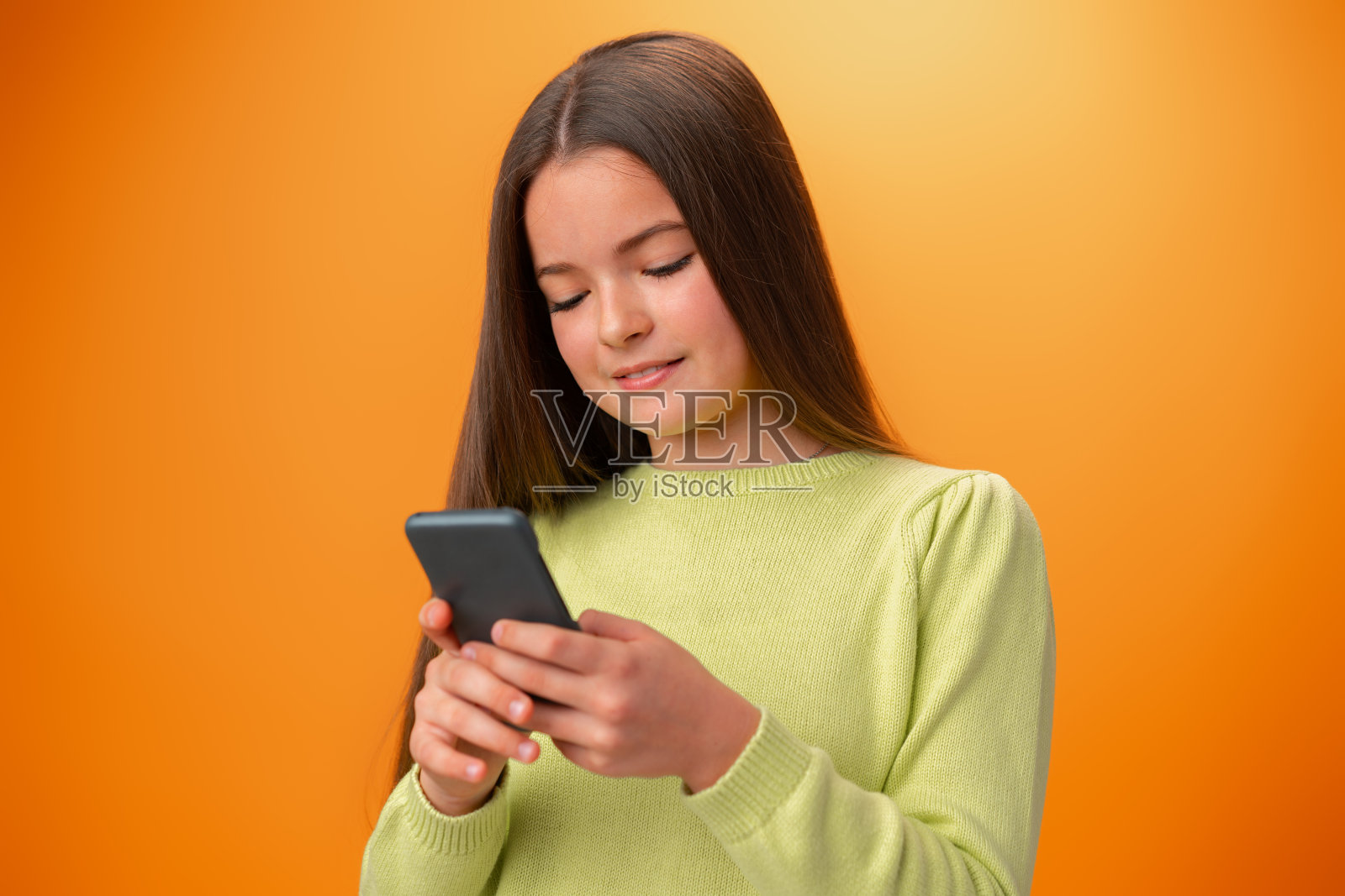 橘色背景下使用手机的可爱少女,面露喜色照片摄影图片