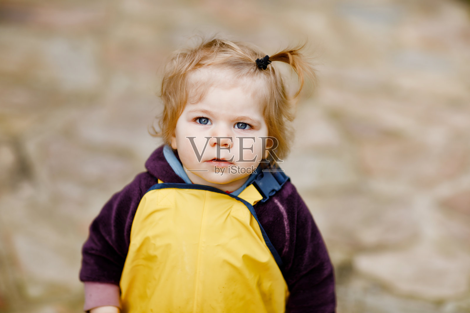 可爱的小女孩在春天的户外玩耍。宝宝穿黄泥雨淋裤。快乐女孩的肖像。照片摄影图片