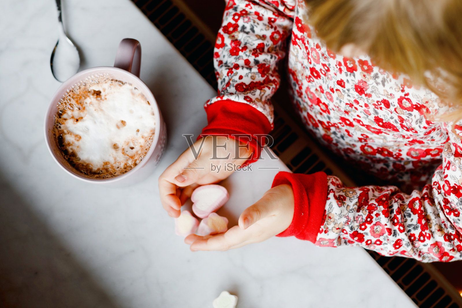 学前班的小女孩拿着杯子,杯子里装着巧克力和棉花糖。快乐的孩子穿着睡衣,在冬天的窗边喝着甜可可。阖家欢度圣诞。照片摄影图片