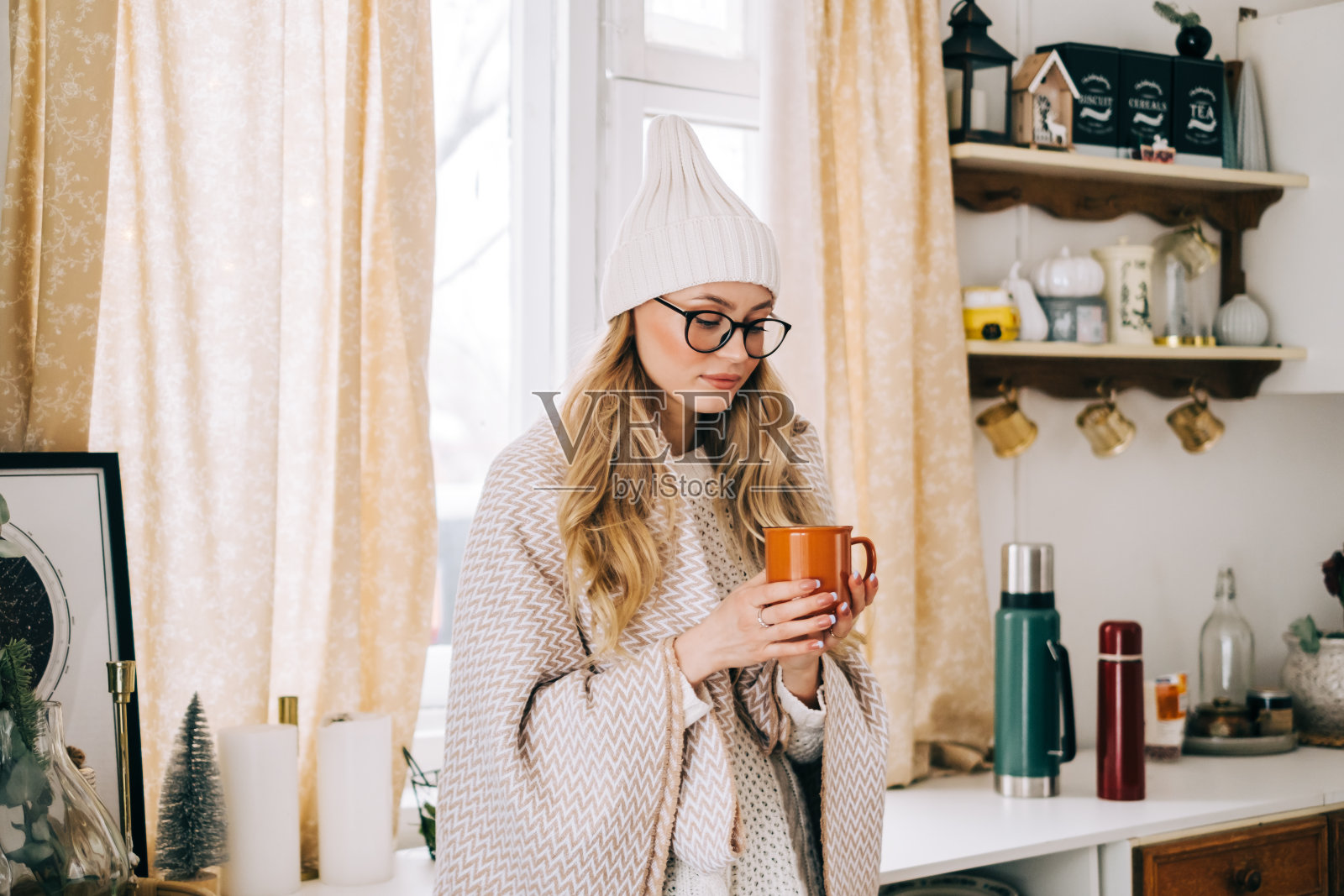 年轻的白人快乐的女人站在厨房和喝茶在冬天的早晨。照片摄影图片