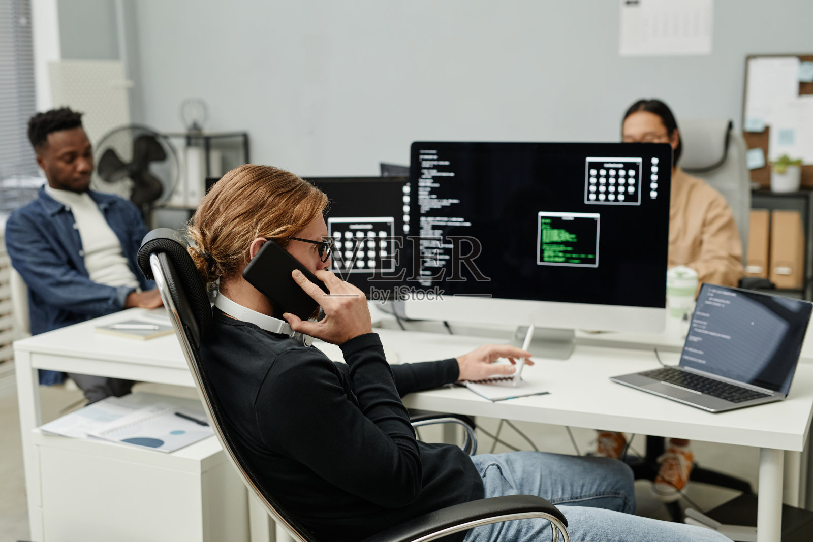 年轻忙碌的程序员坐在电脑前打电话照片摄影图片