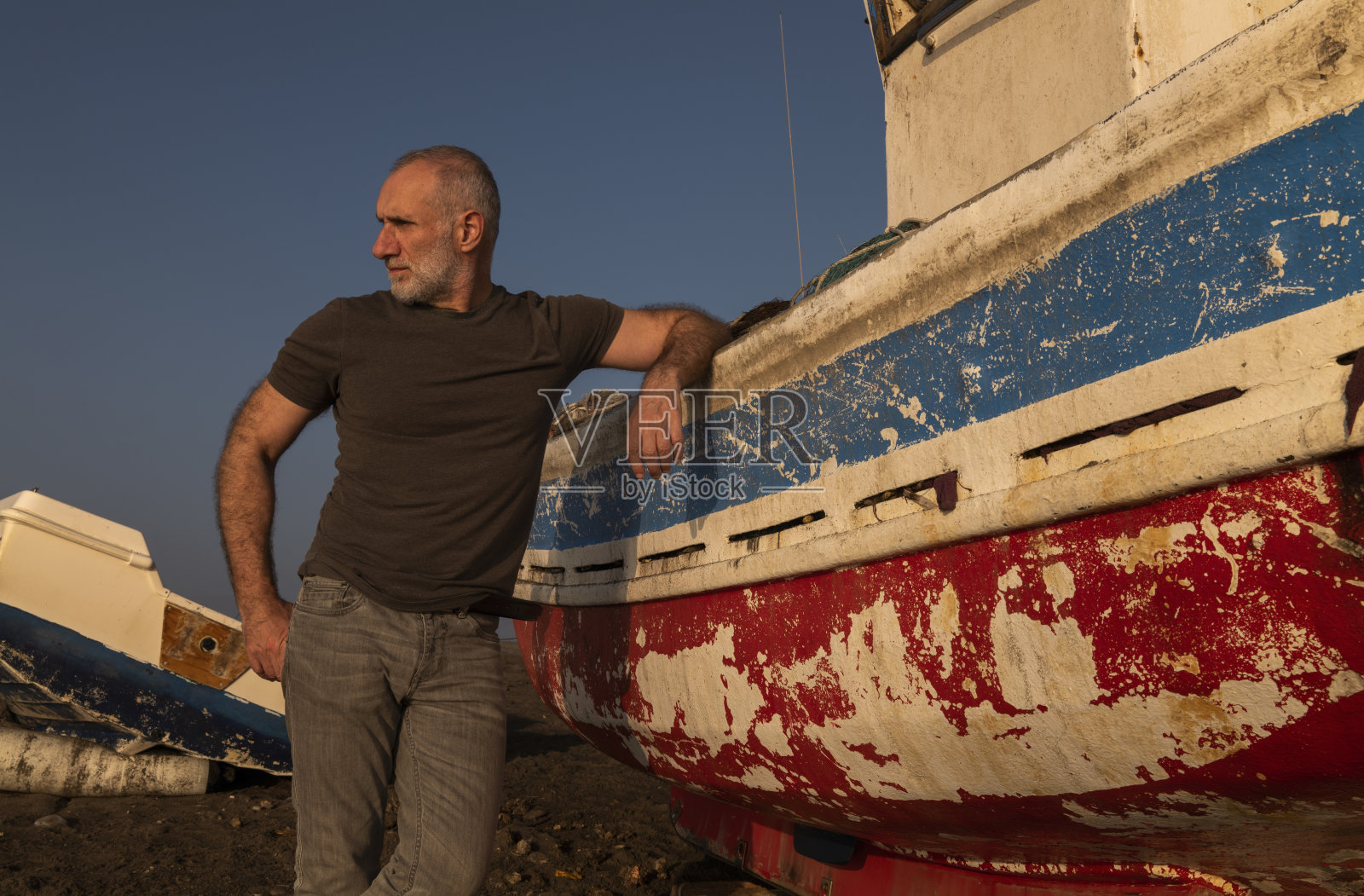 日落时分,一名成年男子和渔船站在海滩上。西班牙阿尔梅里亚照片摄影图片