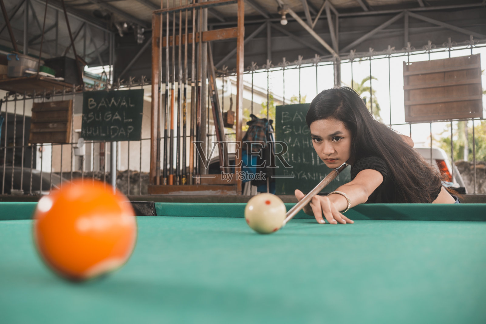 一个漂亮的菲律宾台球运动员练习打9球,目标是5号球。在一个露天的老式台球厅里。照片摄影图片