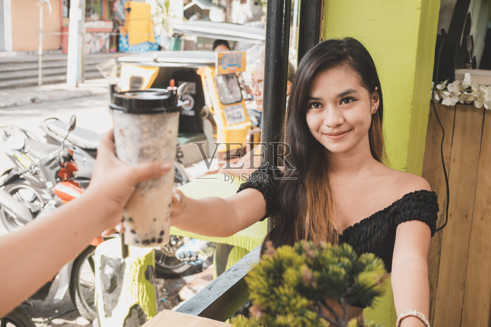 在菲律宾的一家露天咖啡馆里,一位时尚苗条的年轻亚洲青少年穿着露脐上衣喝着珍珠奶茶。照片摄影图片
