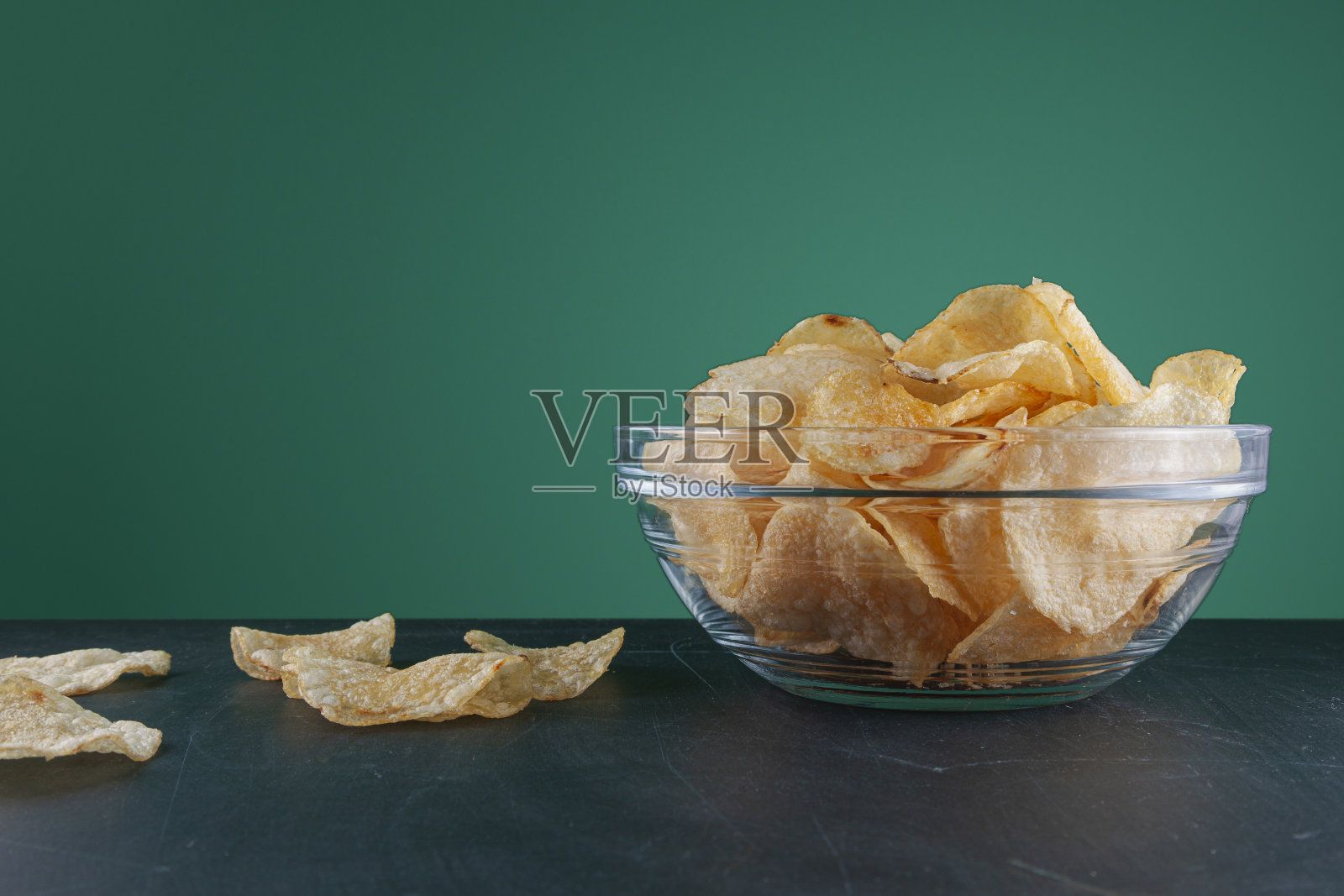 一碗薯片放在有划痕的绿色木头桌子上照片摄影图片