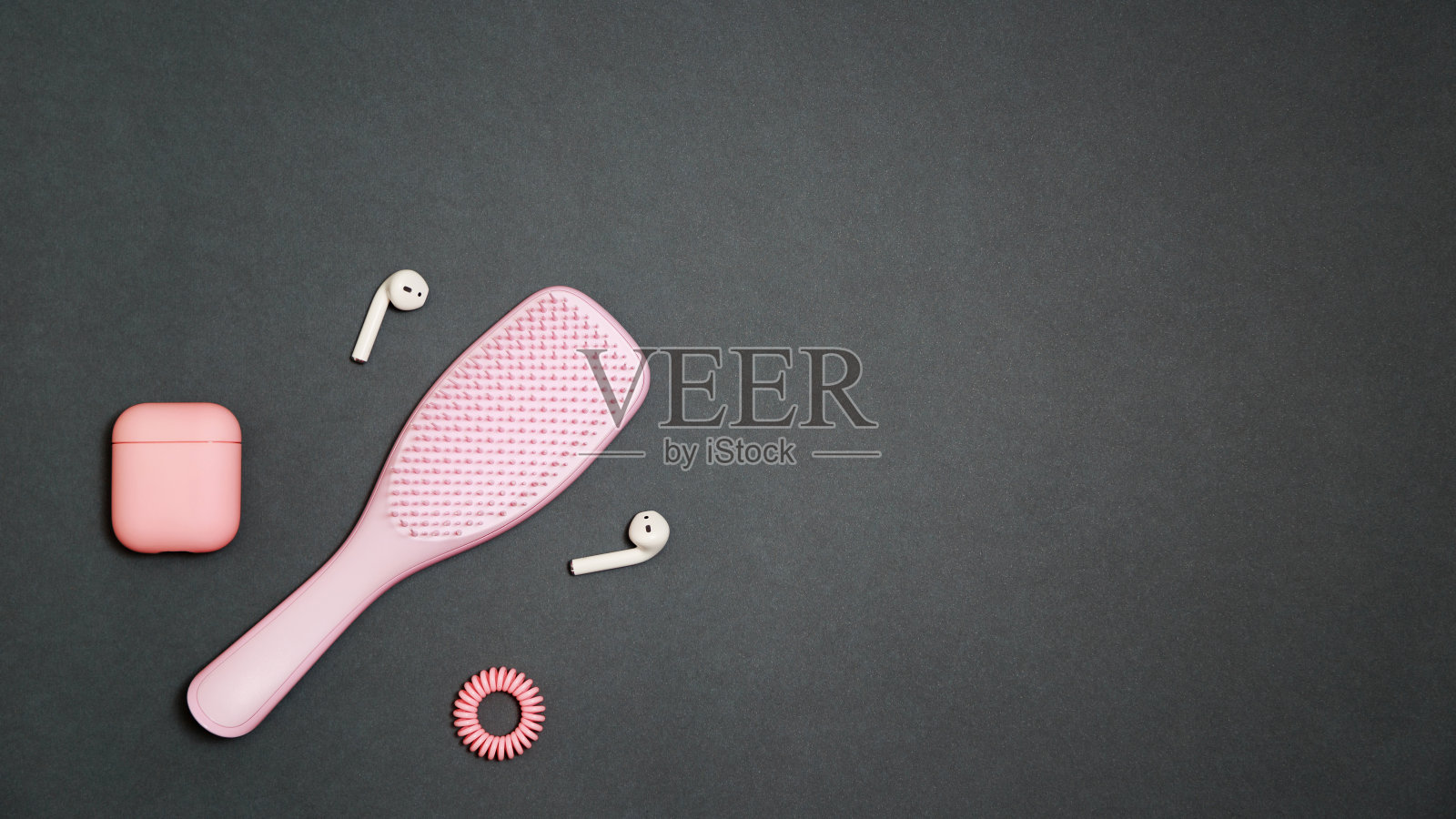 一个时尚的浅粉色女孩的工具包发刷与头发戒指,和扬声器与充电盒在深灰色背景平躺风格的粉红色覆盖照片摄影图片