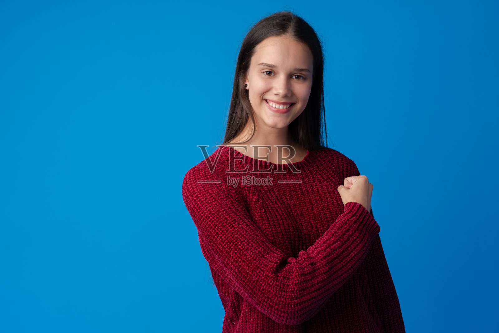 美丽的年轻女子显示她的肌肉和看着镜头在蓝色的背景照片摄影图片