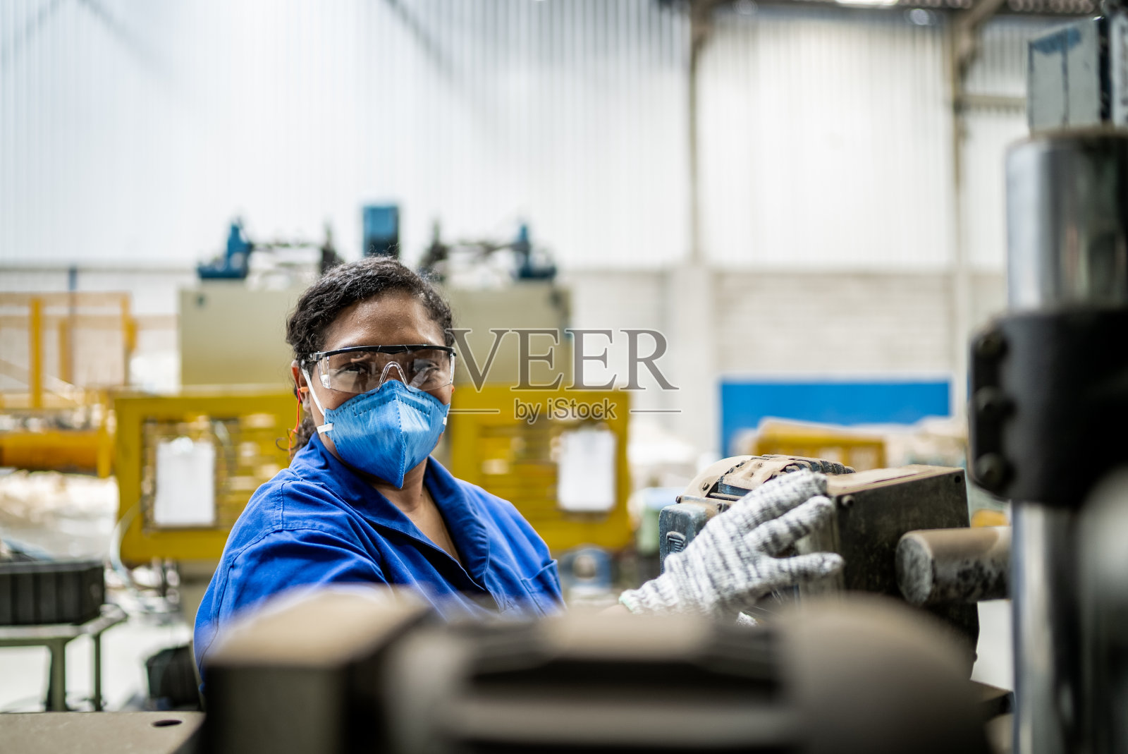 图为一位中年妇女在工厂/工业中工作,戴着防护口罩照片摄影图片