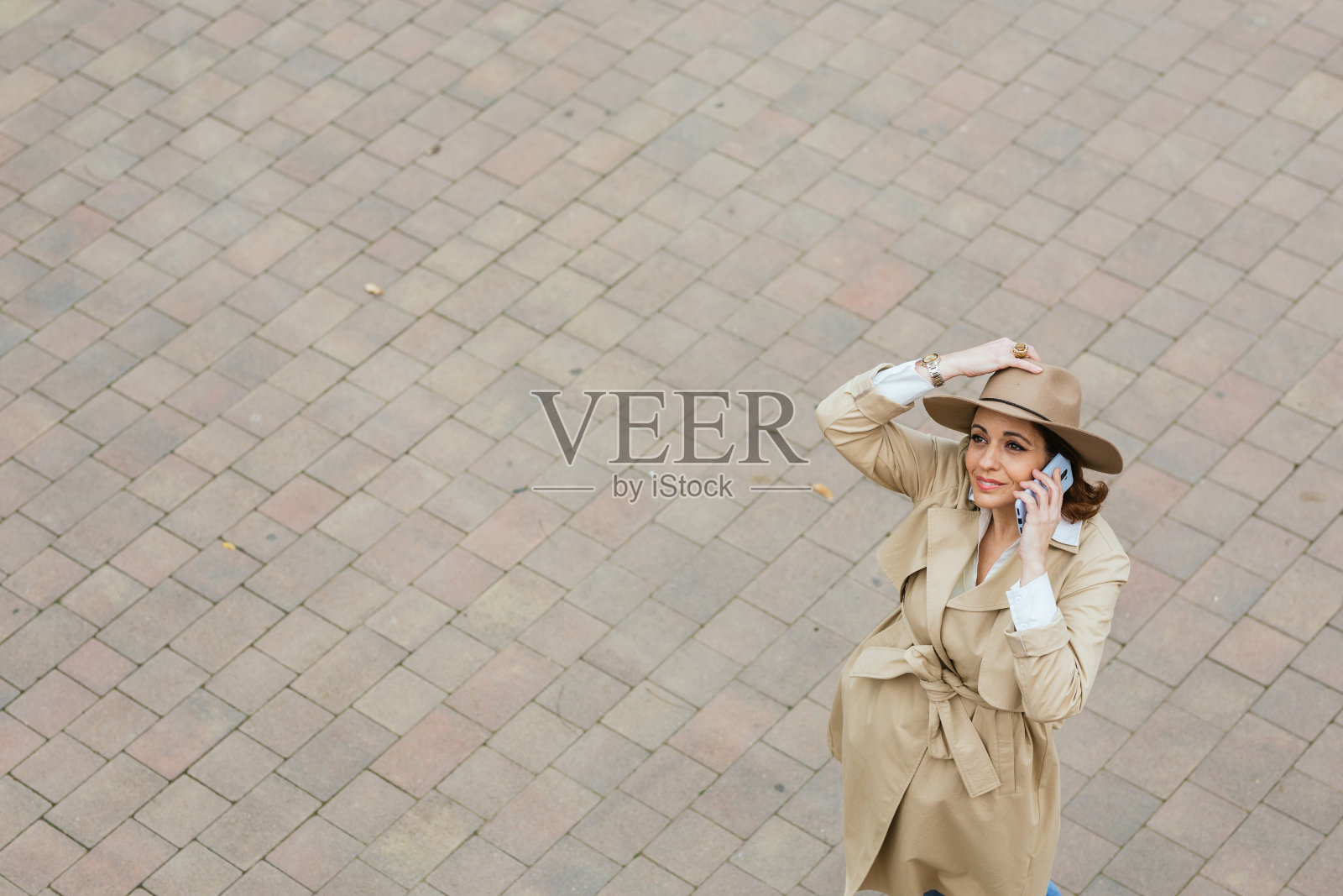 一个戴着帽子,穿着外套的成年女人站在砖石地板上打电话照片摄影图片