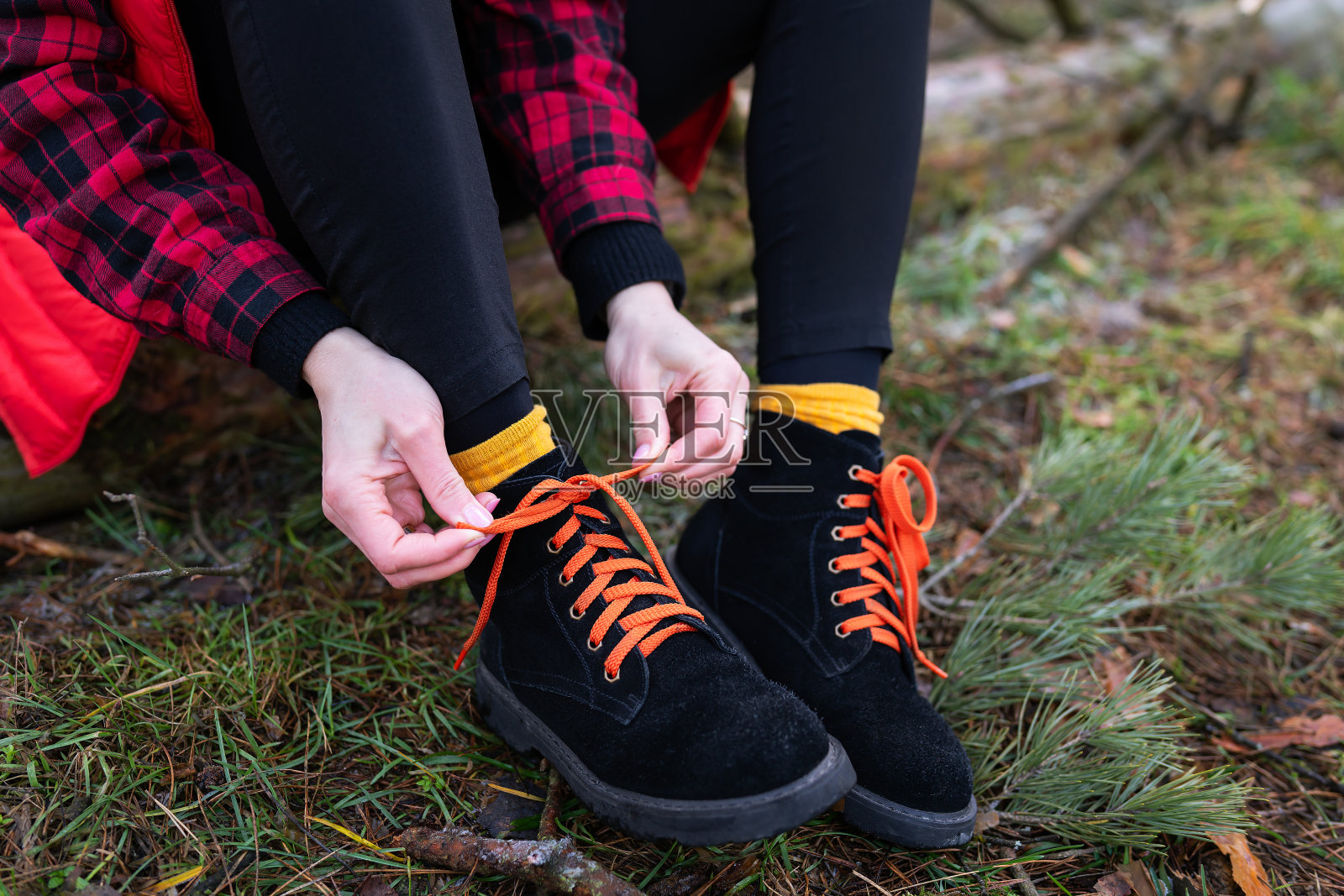 女孩正坐在森林里的一根圆木上系着亮晶晶的鞋带。旅行,徒步旅行和徒步旅行的概念。照片摄影图片