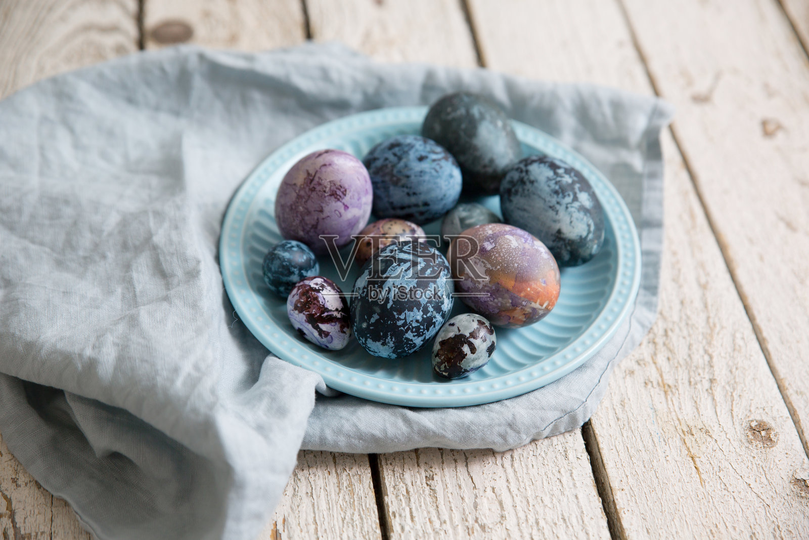 用蓝色、紫色的大理石图案绘制复活节彩蛋。在白色木桌上的蓝色盘子里。照片摄影图片