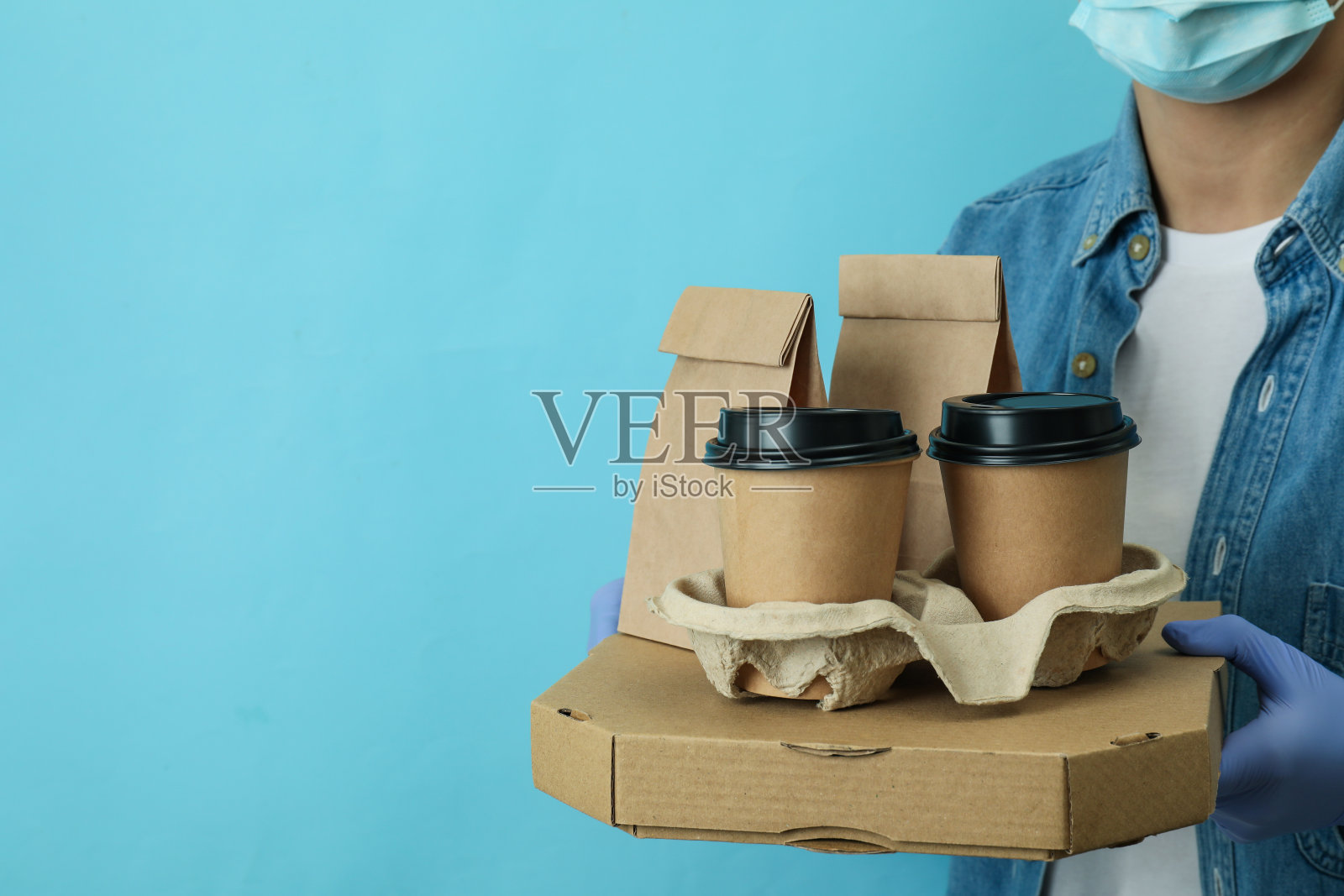 女人拿着装外卖食品的容器,背景是蓝色的照片摄影图片