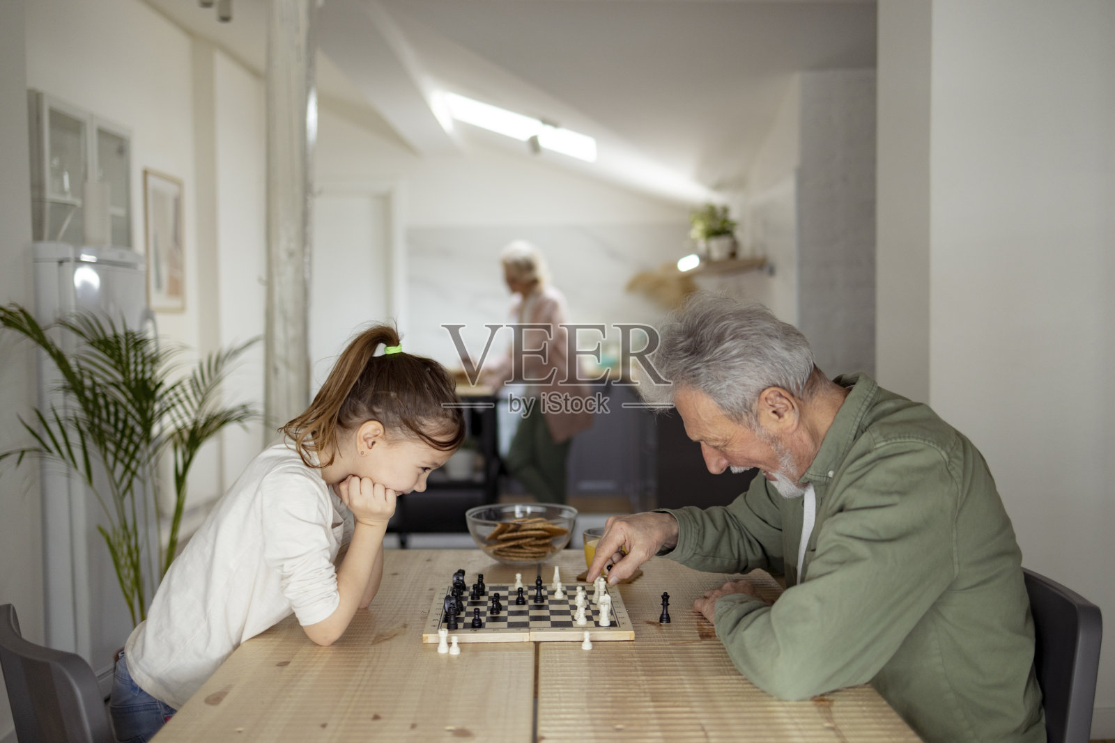 侧视图,一个白人小女孩在家里和她的祖父下棋照片摄影图片