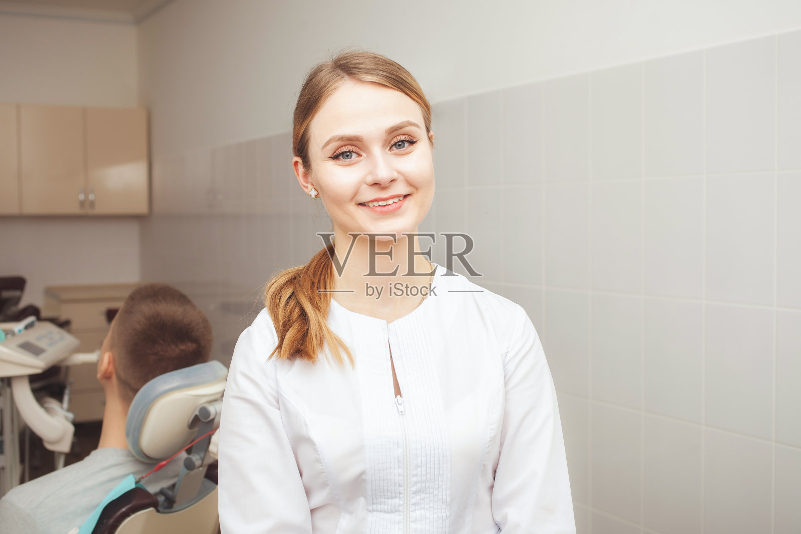 美丽的女医生,牙医的肖像在诊所对背景的病人在办公室。微笑,快乐,整理自己。照片摄影图片