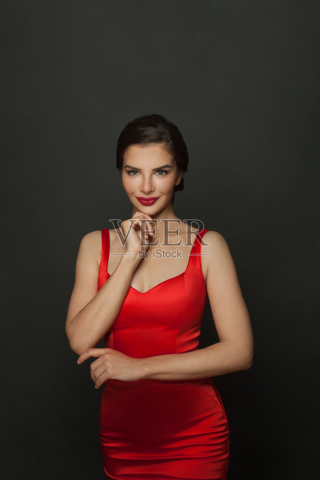 时尚肖像的时尚的女人化妆在红色丝绸连衣裙微笑在黑色的背景。照片摄影图片