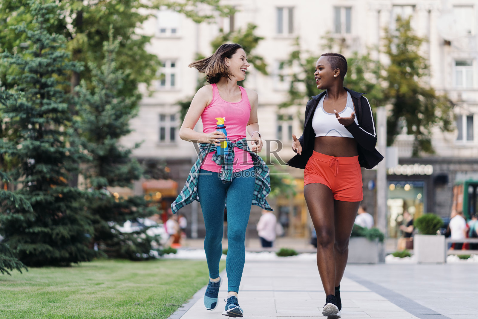 两个多民族女孩跑过城市的街道,在户外交流。照片摄影图片