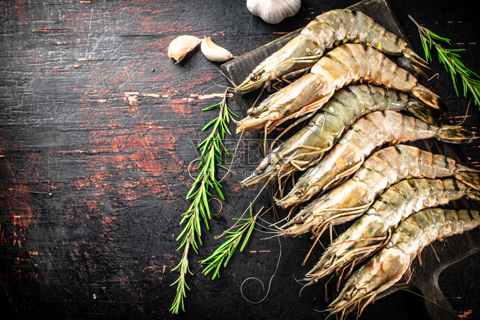 用迷迭香和大蒜把生虾放在切菜板上。照片摄影图片