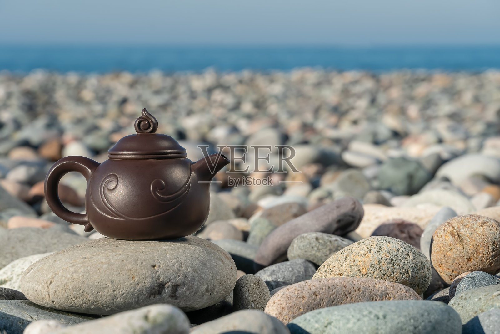 一个棕色茶壶的特写站在石头上卵石海滩的背景,大海在一个阳光明媚的日子,复制空间。茶道的概念照片摄影图片