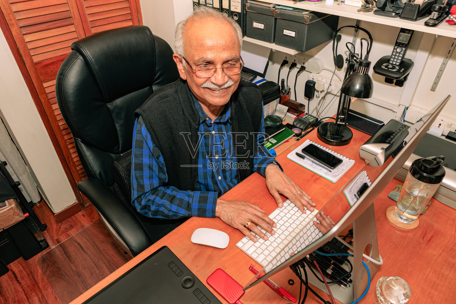 Bogotá,哥伦比亚-一个白发苍苍的74岁亚洲印度人在他的家庭办公室的桌面电脑上工作。照片摄影图片