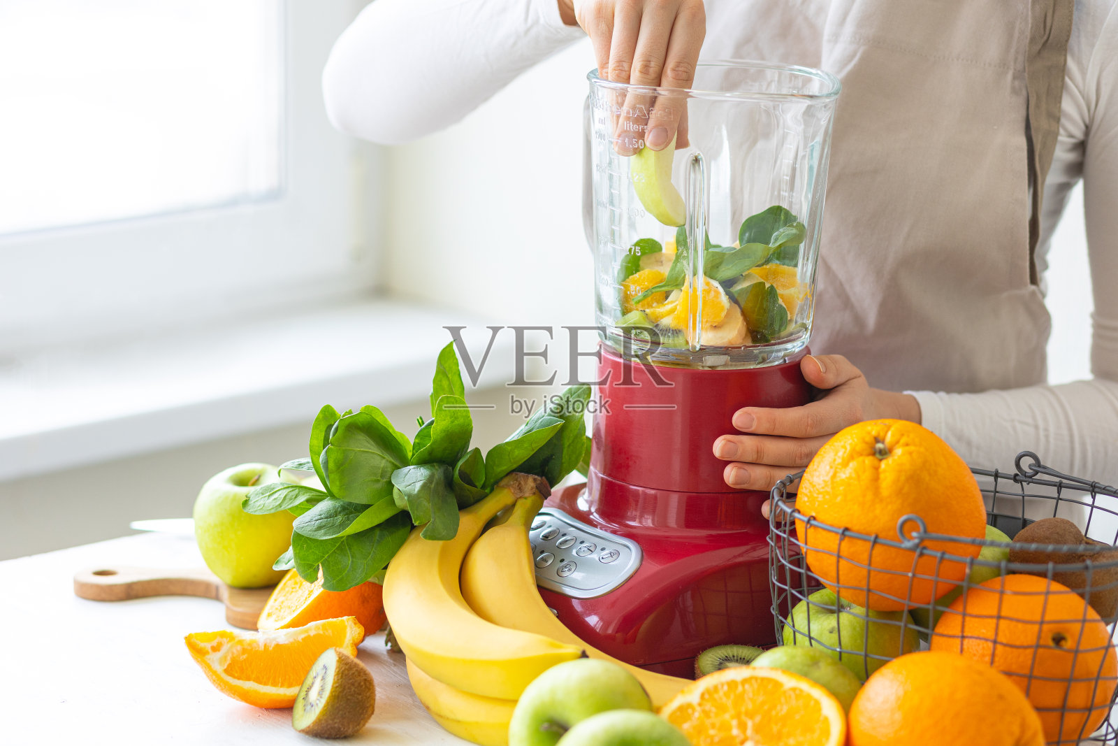 年轻女子正在自制维生素奶昔,里面有苹果,菠菜,香蕉,猕猴桃,橙子。女性的手。健康食品的制备过程。清洁饮食理念,节食,低热量食物。照片摄影图片