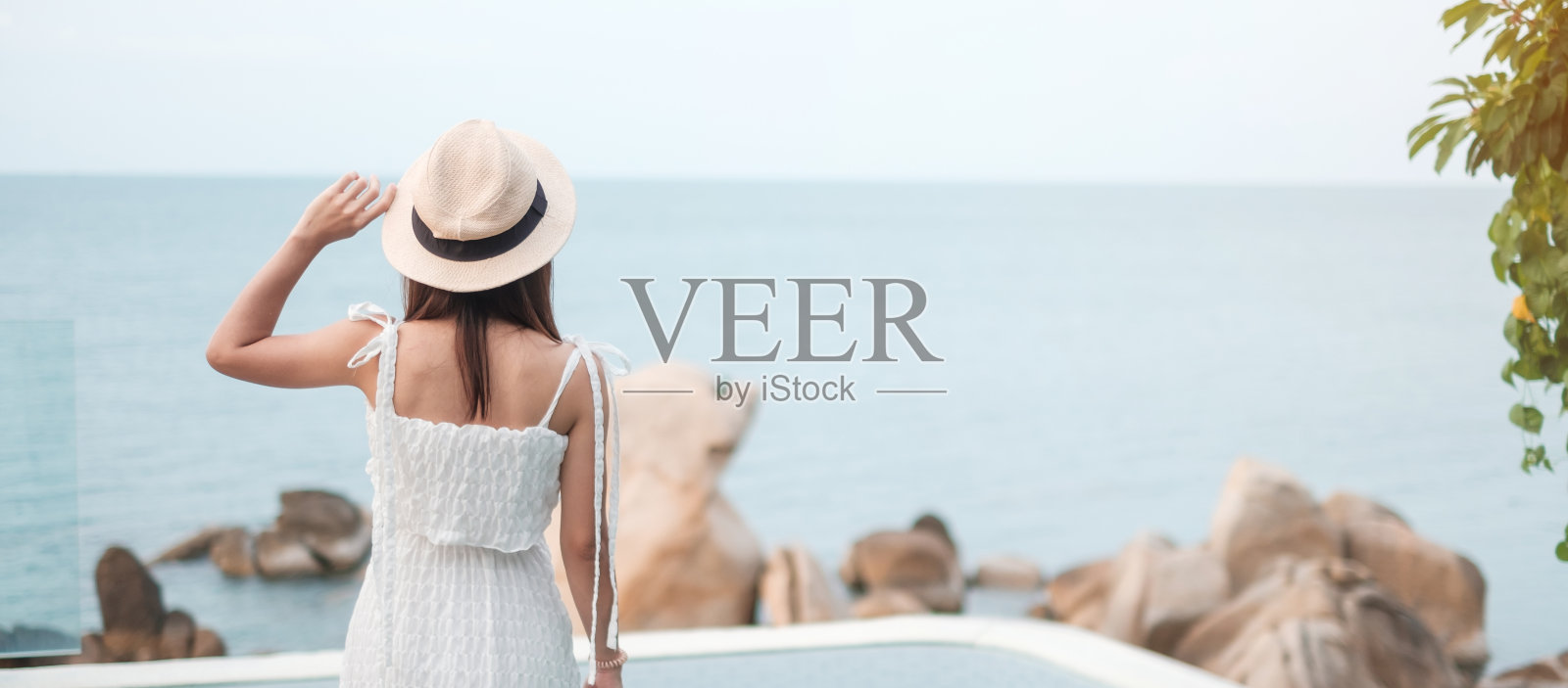 快乐的旅行者女人穿着白色的衣服和帽子享受美丽的海景,年轻的女人站在游泳池。自由、放松、度假、暑假的旅游理念照片摄影图片